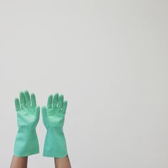 two hands with green gloves on top of each other in front of a white wall