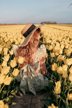 a woman sitting in the middle of a field of yellow tulips wearing a hat