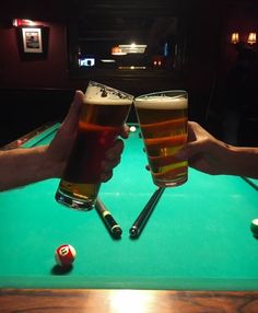 two people toasting with beer at a pool table