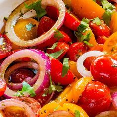 a bowl filled with lots of different colored veggies next to some onions and tomatoes