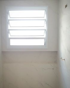 an empty bathroom with white walls and marble flooring, window above the toilet area