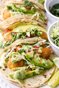 several tacos with guacamole, lime and cilantro on a white plate