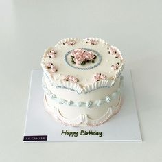 a white cake with pink flowers on top sitting on a card that says happy birthday