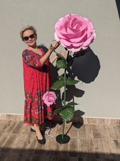 a woman standing next to a giant pink rose