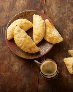 some pastries on a plate next to a cup of coffee and two pieces of bread