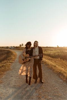 two people standing on a dirt road holding an acoustic guitar