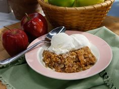 an apple crisp with ice cream on a pink plate next to two baskets of apples