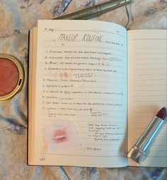 an open book with makeup products on top of it next to a cup of lipstick