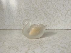 a white swan figurine sitting on top of a marble counter next to a wall