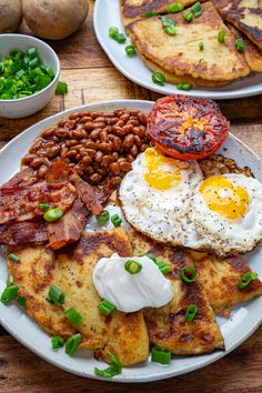 two plates filled with breakfast food on top of a wooden table next to potatoes and eggs