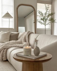 a white couch sitting next to a table with a candle on it and a mirror in the background