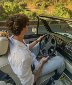 a woman sitting in the driver's seat of a car driving down a road