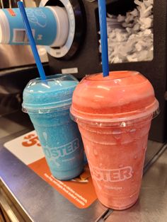 two drinks sitting next to each other on top of a metal counter with blue straws