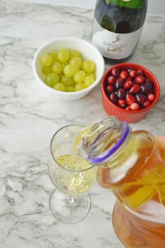 two glasses of wine and some grapes on a marble counter top next to a bottle of champagne