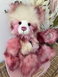 a pink and white teddy bear sitting on top of a table next to some flowers