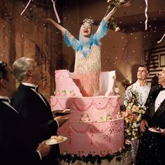 a woman standing on top of a pink cake surrounded by confetti and streamers