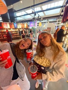 two girls are holding red cups and popcorn