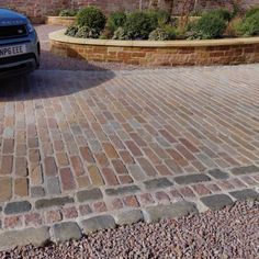 a black car parked in front of a brick driveway with cobblestones on it