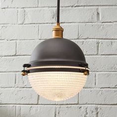 a black and gold light hanging from a brick wall in front of a white brick wall