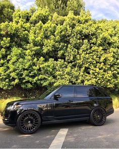 a black range rover parked in front of some trees