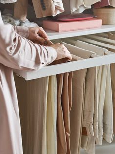 a person standing in front of a shelf with folded clothes on it and holding a book