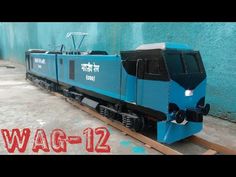 a blue train is parked on the tracks next to a green wall and some words that read wag - 12