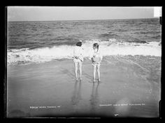 two people standing in the water on a beach next to the ocean with waves coming in