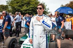 a man standing next to a race car in front of a group of people with umbrellas