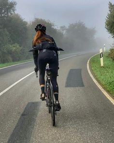 two bicyclists riding down the road on a foggy day in the country