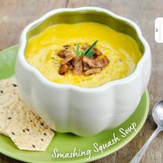 a white bowl filled with soup next to crackers and a spoon on a green plate