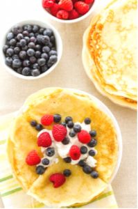 pancakes with berries, blueberries and cream are on a table next to cups of coffee