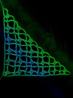 a green crocheted triangle on a black background with blue and green lines in the center