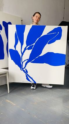 a woman holding up a large blue and white piece of art with leaves on it