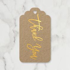 a tag with the words thank you gold foiled on it, sitting on a marble surface