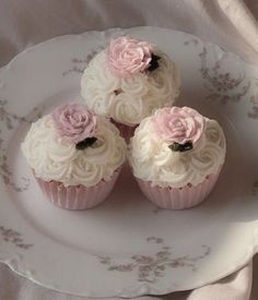 three cupcakes with white frosting and pink flowers on a floral china plate