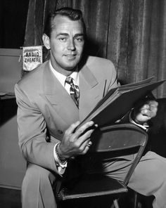 a man in a suit and tie sitting on a chair holding an open file folder