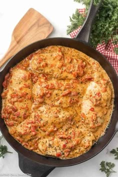 a skillet filled with meat and sauce on top of a table next to parsley