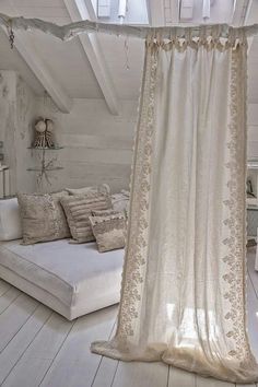 a white bed sitting under a window next to a wooden floor covered in pillows and blankets