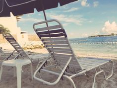 two lawn chairs sitting on top of a sandy beach next to the ocean with an umbrella over them