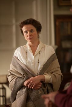 the woman is wearing a white shirt and brown shawl while sitting in a chair