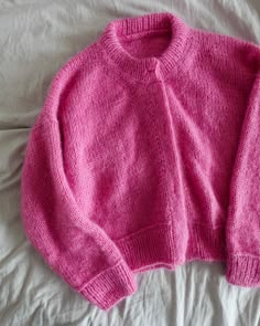 a pink sweater laying on top of a bed