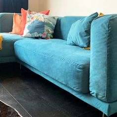 a blue couch with pillows on it in front of a window and black rugs