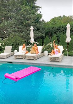 three women lounging on lounge chairs next to a swimming pool with an inflatable floater