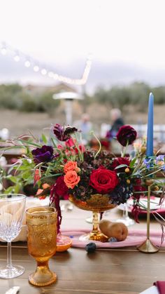 a wooden table topped with lots of flowers next to wine glasses and candle holders on top of it