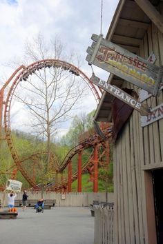 the entrance to an amusement park with a roller coaster in the background and people walking around