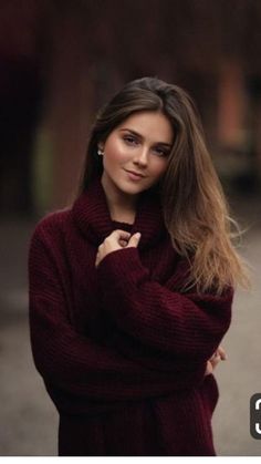 a woman with long hair wearing a sweater and posing for a photo in the street