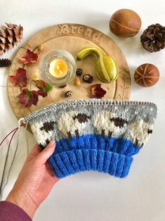 a person holding up a knitted mitt next to pine cones, nuts and an orange