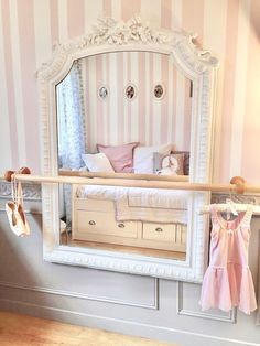 there is a mirror on the wall with clothes hanging in front of it and a baby's pink dress