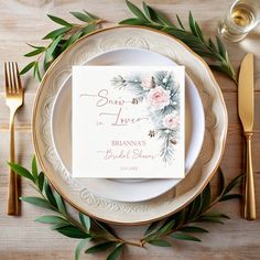 a place setting with flowers and greenery on the plates, gold cutlery and silverware