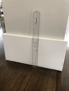 a white box with a ruler sticking out of it's side on a wooden floor